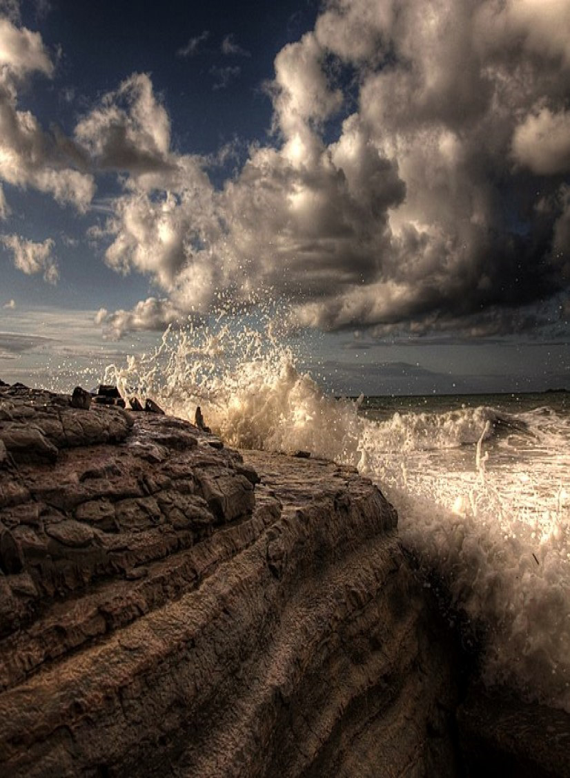 Stock image of stormy clouds and strong waves crashing against a cliff